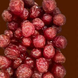 A small pile of bright red dried cherries on a neutral surface, showing their wrinkled texture.